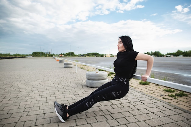 Foto giovane donna che fa push up sulla barra orizzontale all'esterno. donna che si allena vicino allo stadio. concetto di fitness, sport, esercizio e stile di vita.