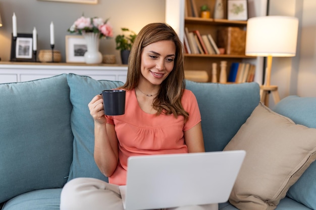 Young woman doing research work for her business Smiling woman sitting on sofa relaxing while browsing online shopping website Happy girl browsing through the internet during free time at home