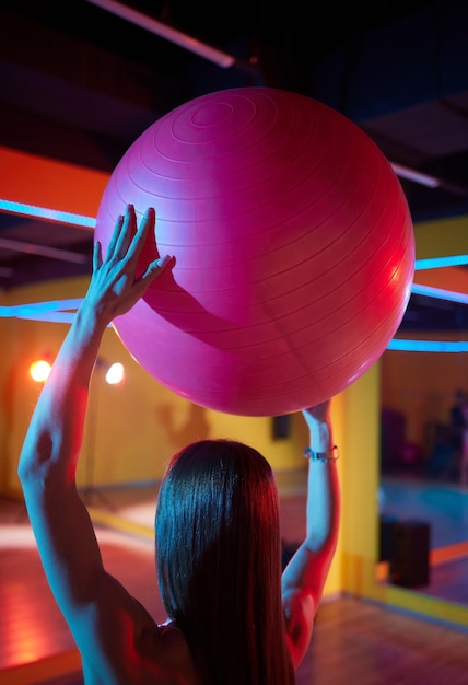 Young woman doing side stretch pilates mermaid exercises with a gym ball working out in front of a mirror in a gym