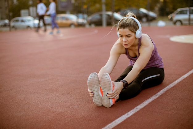 Young woman doing some exercises and streching legs at the court at outdoor