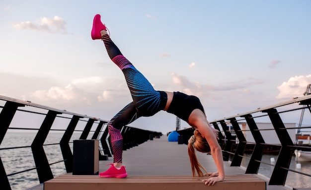 Young woman doing sports exercises at dawn near the ocean