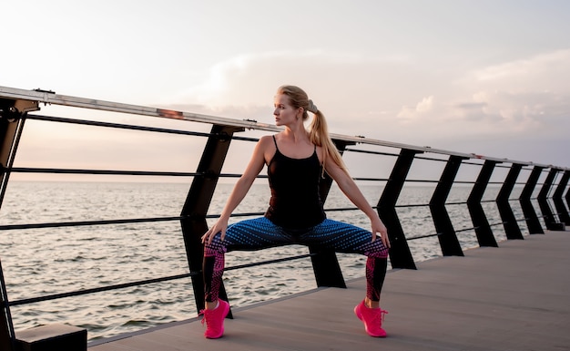 Young woman doing sports exercises at dawn near the ocean