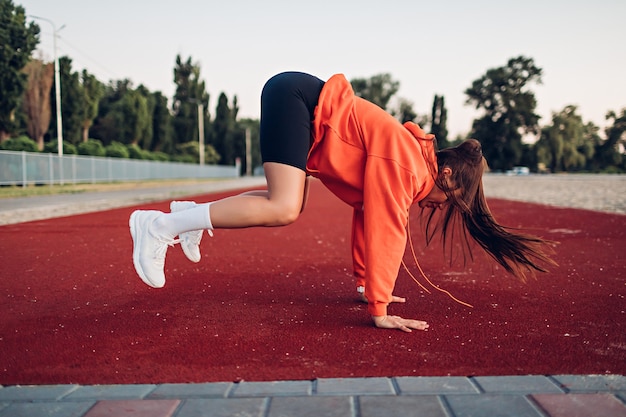 Young woman doing warmup exercises on sportsground early in the morning