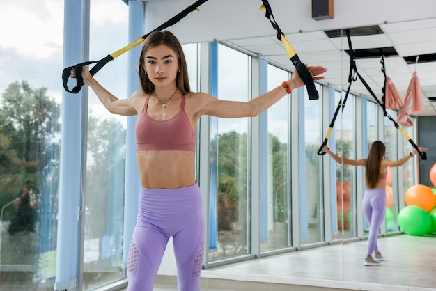 Young woman doing workout with trx straps training arms in fitness gym. Sport for healthy lifestyle.