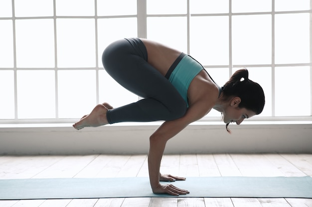 Foto giovane donna che fa esercizio di asana di yoga al chiuso vicino alla finestra