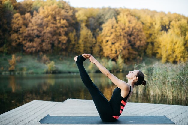 Young woman doing yoga asana in nature near the lake