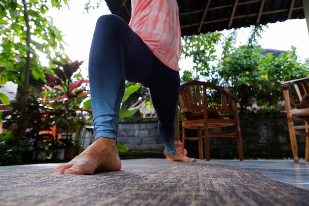 Young woman doing yoga asana Virabhadrasana Warrior Pose outside on terrace during vacation