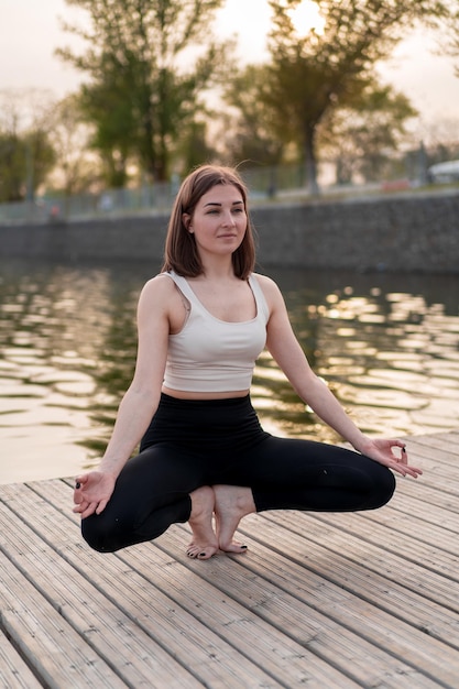 Giovane donna che fa yoga in riva al lago