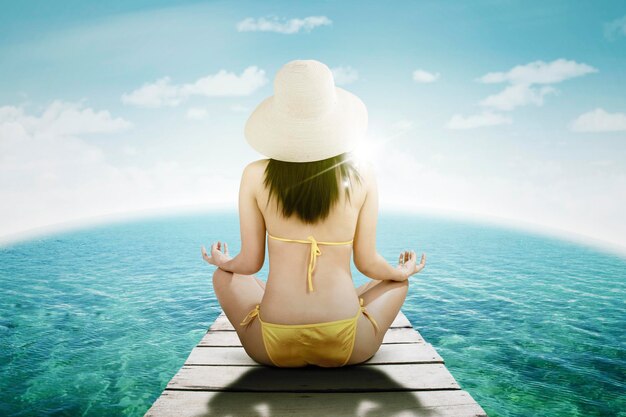 Young woman doing yoga exercise on wooden jetty