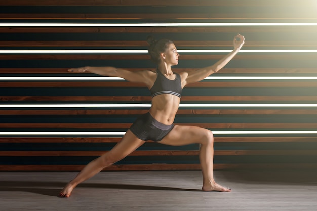 Young woman doing yoga exercises in dark studio. Health lifestyle concept.