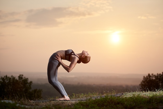 Young woman doing yoga exercises outdoors at sunset