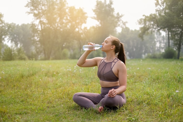 夏の公園でマットの上でヨガをしている若い女性。健康的なスポーツライフスタイルのコンセプト。アクティブでアスレチックな女性のエクササイズ