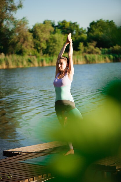 Foto giovane donna che fa yoga nel parco di mattina vicino al lago.