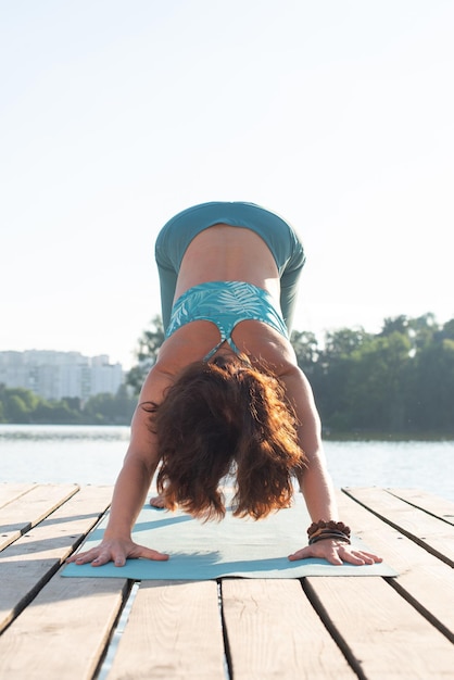 Young woman doing yoga on the pier near the river