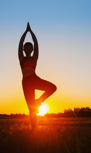 Young woman doing yoga at sunset in summer