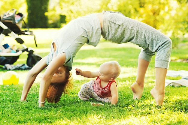 Young woman doing yoga with baby in the summer parkFamily outdoors Parent with child