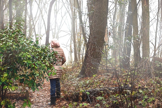 A young woman in a down coatjacket is walking through a foggy forest