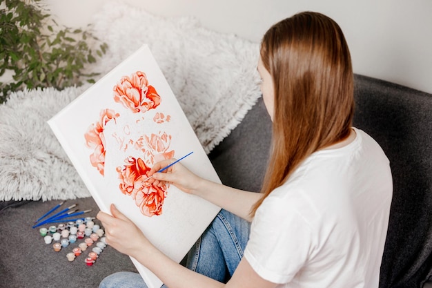 Young woman drawing picture by numbers with acrylic paints on canvas