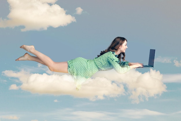 Young woman in dress flying with laptop in the sky