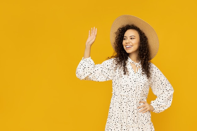 Young woman in dress and hat on yellow background