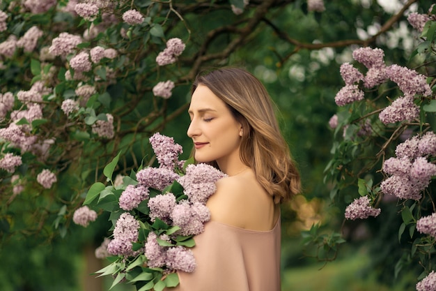 Young woman in a dress is standing near a lilac bush