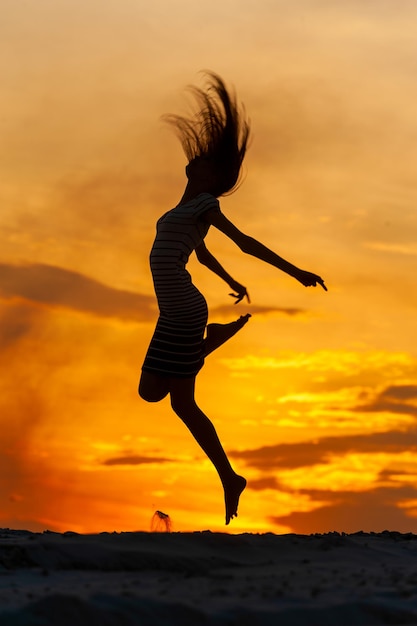 Foto giovane donna in vestito che salta al tramonto.