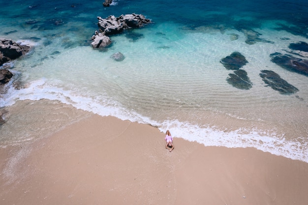 Young woman in a dress lying on the back on the white sand near the waves of blue sea. Top view, Andaman Sea, Phuket, Thailand. Aerial