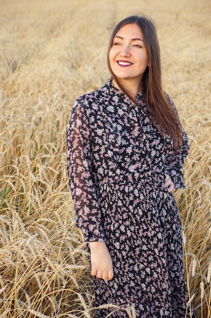 Young woman in a dress stands in a wheat field.