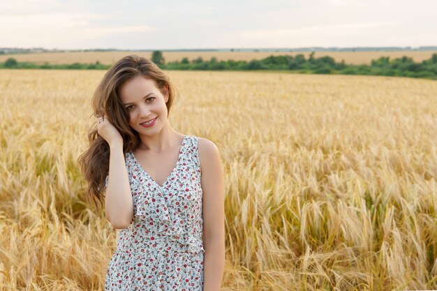 Giovane donna in abito sul campo di grano estivo. ragazza sorridente sul prato dorato. libertà