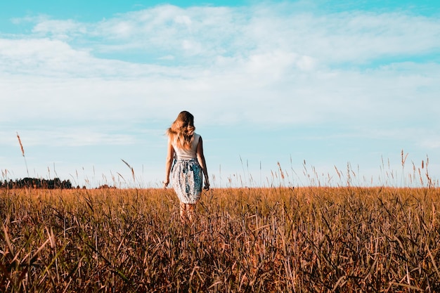 Young woman in dress walking along cereal field