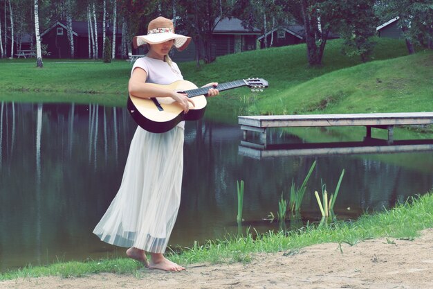 湖の近くのギターとドレスの若い女性