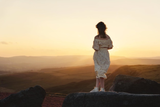 夏の日没の丘の上にラベンダーのブーケを手にしたドレスを着た若い女性