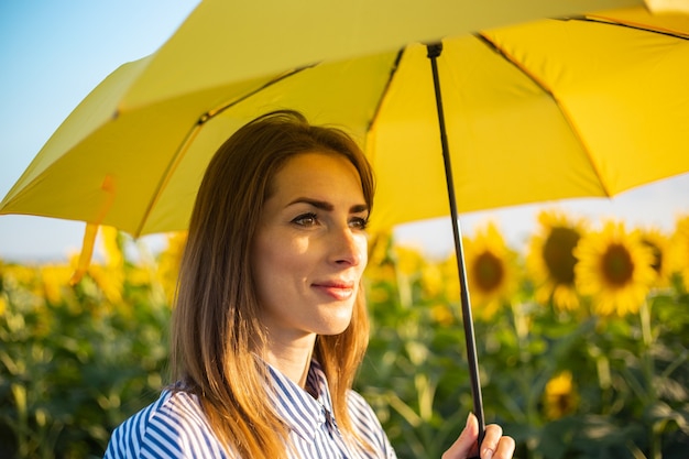 Young woman in dress and yellow umbrella on a field of sunflowers.