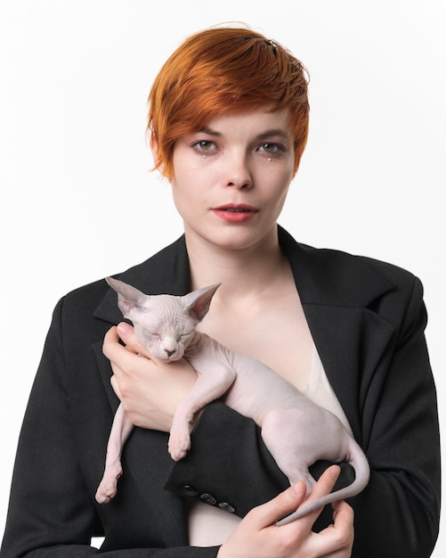 Young woman dressed in black jacket holding in hands sleeping Sphynx kitten