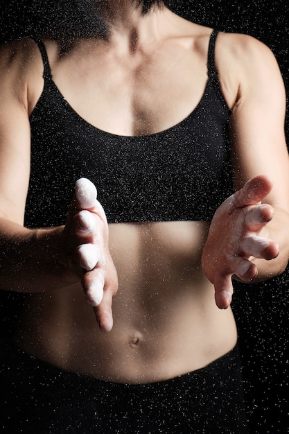 Young woman dressed in a black top claps in her hands with white magnesia