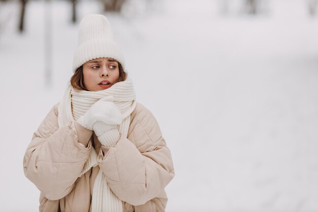 写真 若い女性がコートスカーフ帽子手袋を着て雪に覆われた冬の公園で冬の天気を眺めています