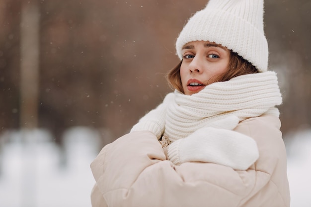 Foto giovane donna vestita con un cappotto, una sciarpa, un cappello e guanti e il tempo invernale nel parco invernale innevato