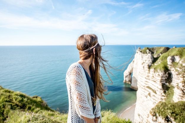 Young woman dressed in hippie style enjoying nature on the rocky coastline with great view on the ocean in France