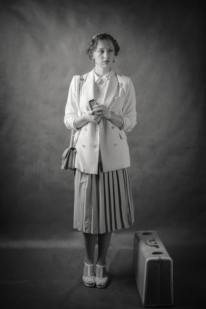 Фото Молодая женщина, одетая в стиле ретро, с чемоданом и книгой в руках. студийный портрет