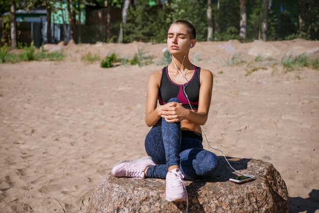 Young woman dressed in sportswear sits on beach for learning music listening