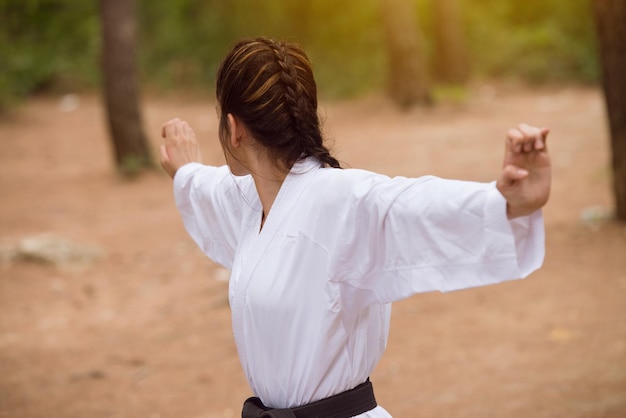 전통 기모노를 입은 젊은 여성이 숲이 우거진 숲 지역 블랙 벨트에서 가라테 동작을 연습합니다.