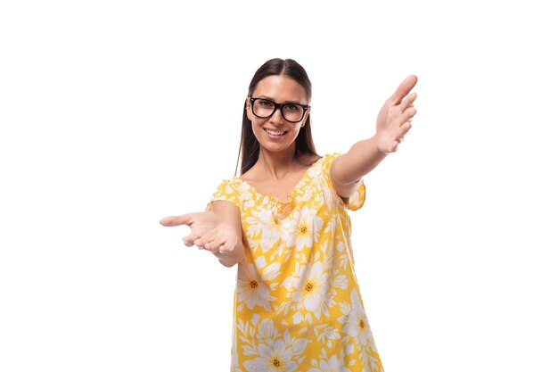 A young woman dressed in a yellow sundress and with glasses rejoices and smiles