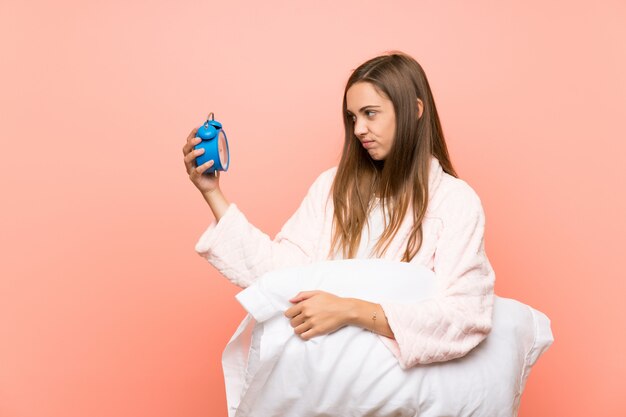 Young woman in dressing gown over pink wall holding vintage clock