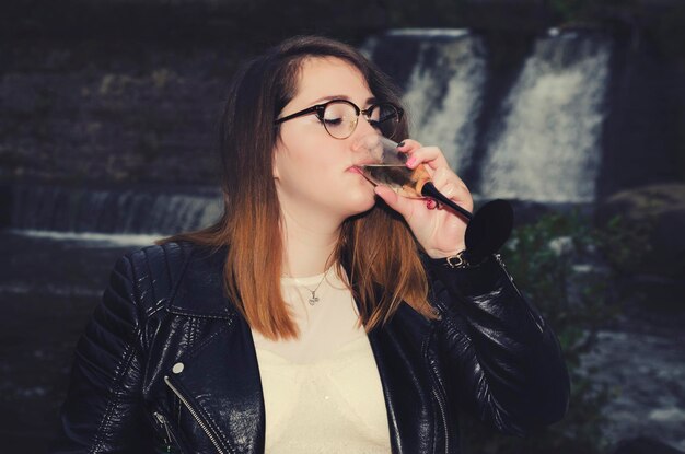 Foto giovane donna che beve champagne contro la cascata