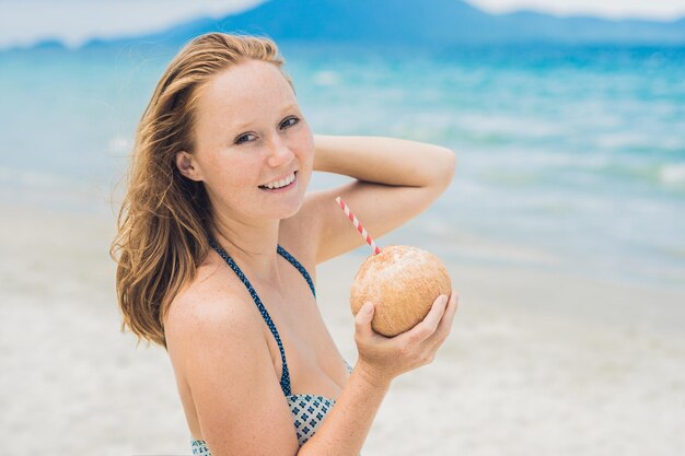 Giovane donna che beve latte di cocco sulla spiaggia. scape da sogno fuga con la ragazza di bellezza. i benefici dell'acqua di cocco.