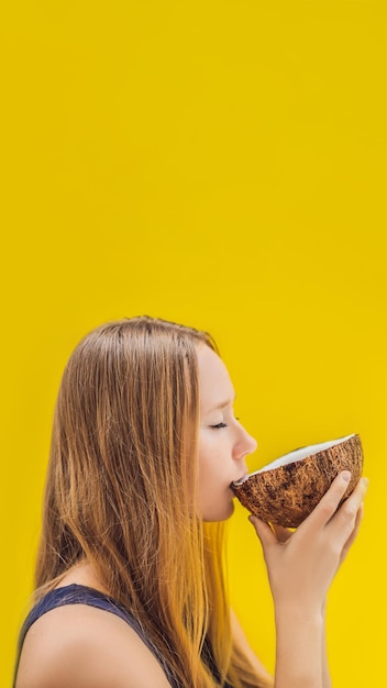 Foto giovane donna che beve latte di cocco sulla noce di cocco chafrom su un formato verticale di sfondo giallo per