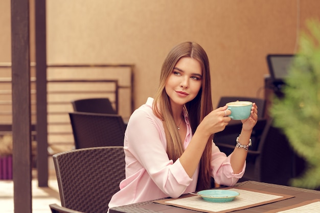 Giovane donna che beve il caffè in un caffè all'aperto