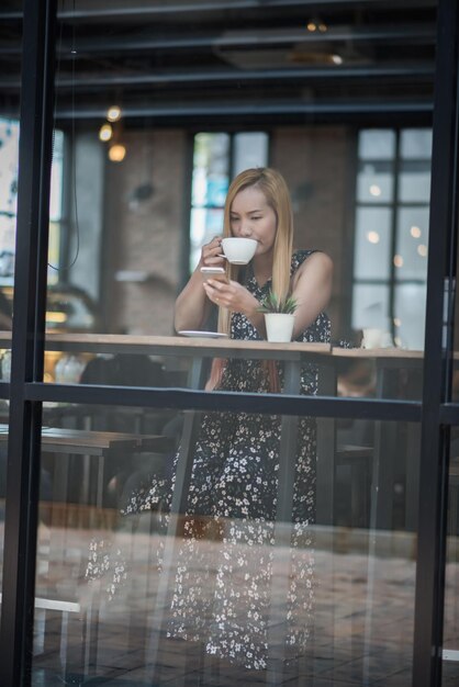 Photo young woman drinking coffee in cafe while using mobile phone