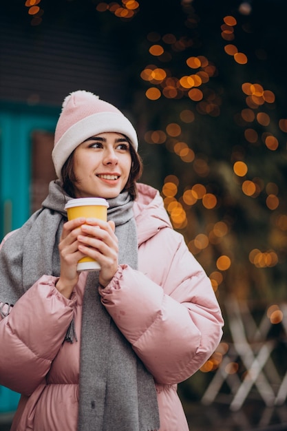 Молодая женщина пьет кофе за пределами зимней улицы