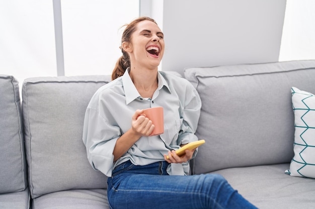 Young woman drinking coffee and using smartphone at home